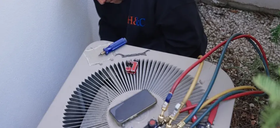 H&C technician checking refrigerant pressures on a central AC condenser